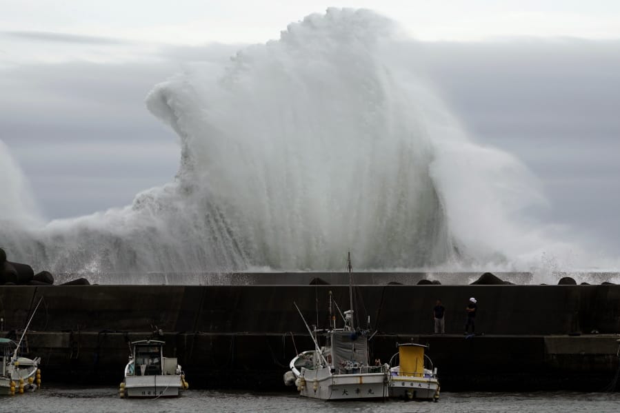 Men look at fishing boats as surging waves hit against the breakwater while Typhoon Hagibis approaches at a port in town of Kiho, Mie Prefecture, Japan Friday, Oct. 11, 2019. A powerful typhoon is advancing toward the Tokyo area, where torrential rains are expected this weekend.