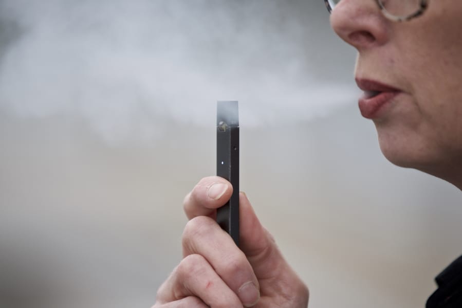 FILE - In this April 16, 2019, file photo, a woman exhales a puff of vapor from a Juul pen in Vancouver, Wash. A former Juul Labs executive is alleging that the vaping company knowingly shipped 1 million tainted nicotine pods to customers. The allegation comes in a lawsuit filed Tuesday, Oct. 29, by a former finance executive who was fired by the vaping giant earlier this year.