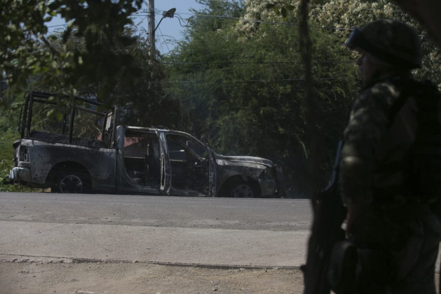 A soldier stands by a charred truck that belongs to Michoacan state police, after it was burned during an attack in El Aguaje, Mexico, Monday, Oct. 14, 2019. At least 13 police officers were killed and three others injured Monday in the ambush.