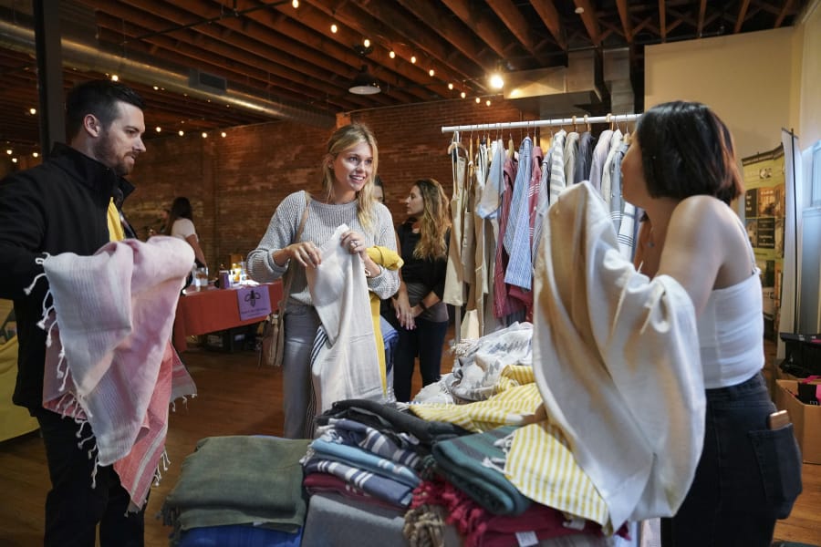 Seth Alcott, left, and his wife, Noelle Alcott, of Vancouver decide on a Turkish towel with the help of Elif Sari Genc, right, the owner of Hands on Hips, a Turkish towels and textiles shop, at the Night Market Vancouver last year.