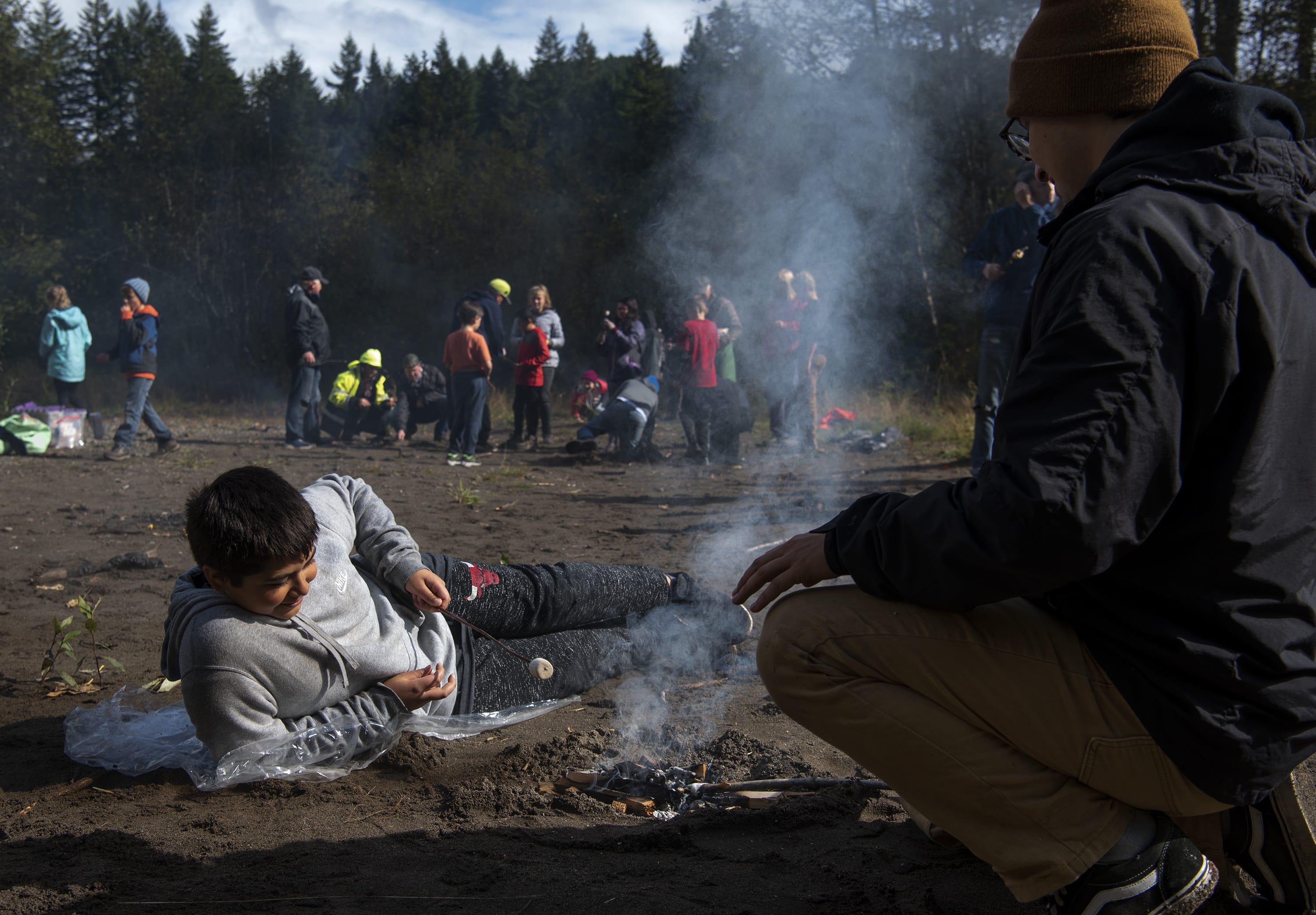 Sunset Ridge Intermediate School fifth-grader Jacob Springer, left, and Ridgefield High School senior Isaac Moreno, right, roast marshmallows and tend to a fire during the fire building workshop at the Cispus Learning Center outdoor program in Randle on Tuesday, Oct. 8, 2019. The students had workshops and field study sessions covering topics like astronomy, geology, nature writing, and outdoor survival skills.