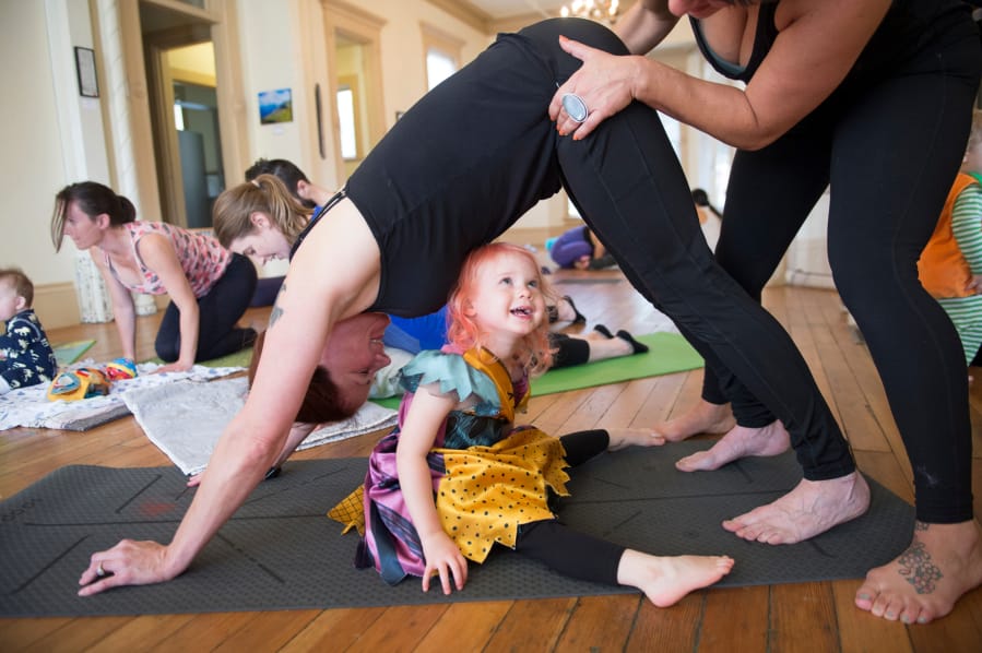 Saffron Smith, 2, looks up while yoga teacher Daniele Strawmyre helps her mother, Jennifer Smith, with a downward dog pose during a Ready Set Grow yoga class at the Slocum House in Esther Short Park on Saturday, October 26, 2019. Ready Set Grow is a yoga studio based in Portland and Vancouver.