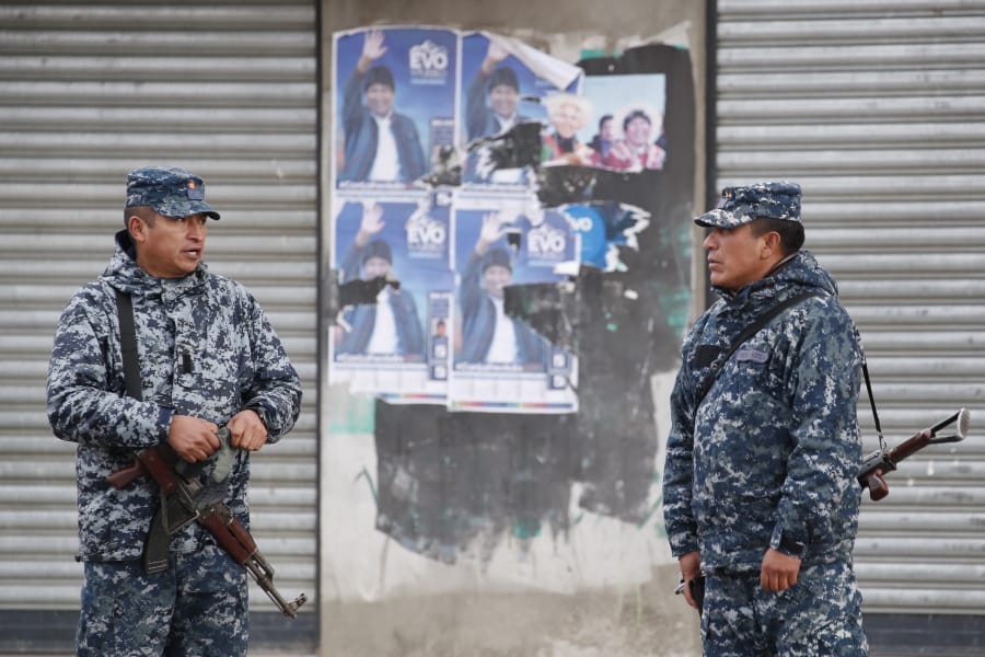 Soldiers stand in front of electoral posters of former President Evo Morales in El Alto, outskirts of La Paz, Bolivia, Tuesday, Nov. 12, 2019. Bolivia faced political vacuum Tuesday, while Morales fled the country on a Mexican plane following weeks of widespread protests fed by allegations of electoral fraud in the Oct.