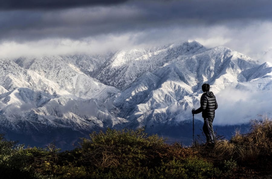 Frank Huong takes a break from hiking to enjoy a view of snow-capped San Gabriel Mountains from Hidden Hills trail in Chino Hills, Calif.,  on Friday, Nov. 29, 2019.  Rain and snow showers are continuing in parts of the state Friday morning while skies are clearing elsewhere.