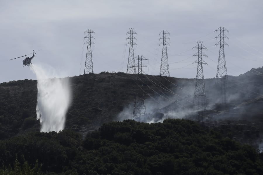 FILE - In this Oct. 10, 2019, file photo, a helicopter drops water near power lines and electrical towers while working at a fire on San Bruno Mountain near Brisbane, Calif. California&#039;s Pacific Gas &amp; Electric is faced regularly with a no-win choice between risking the start of a deadly wildfire or immiserating millions of paying customers by shutting off the power.
