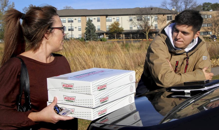 In this Saturday, Oct. 26, 2019 photo, Catherine Newton, left, buys three boxes of Krispy Kreme doughnuts from Jayson Gonzalez in Little Canada, Minn. Gonzalez, a Minnesota college student, says Krispy Kreme has told him to stop making doughnut runs to Iowa. Gonzalez told the Pioneer Press he was told his sales created a liability for the North Carolina-based company.