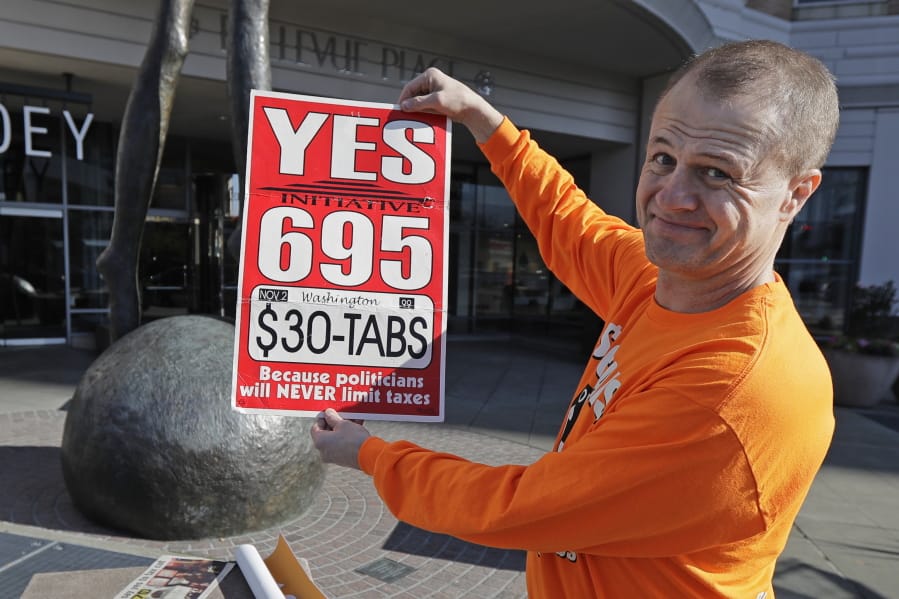 Anti-tax activist Tim Eyman poses for a photo with a sign from his original 1999 campaign for $30 car registration tabs, Tuesday, Nov. 5, 2019, as he waved a sign for his current Initiative 976 on election day in Bellevue, Wash. The measure would again cut most car tabs to $30 in Washington state, if passed by voters, and would leave state and local governments scrambling to pay for road paving and other transportation projects. (AP Photo/Ted S.