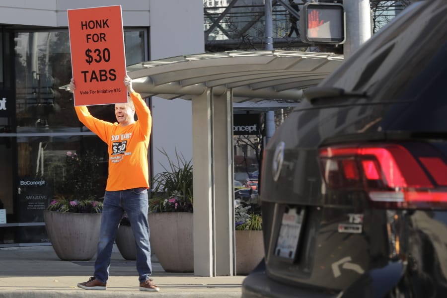 Anti-tax activist Tim Eyman holds a sign supporting Initiative 976, which would cut most car registration tabs to $30 in Washington state, Tuesday, Nov. 5, 2019, on election day in Bellevue, Wash. If passed by voters, the measure would leave state and local governments scrambling to pay for road paving and other transportation projects. (AP Photo/Ted S.