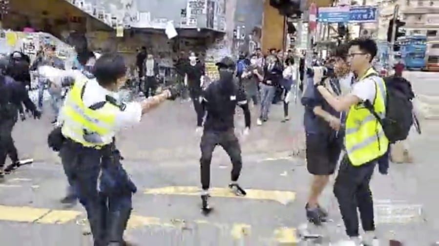 In this image made from video, a police officer, left, prepares to shoot a protester, center, in Hong Kong Monday, Nov. 11, 2019. The police shot the protester as demonstrators blocked subway lines and roads during the Monday morning commute.