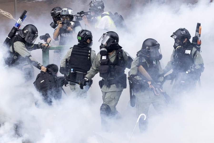 Police in riot gear move through a cloud of smoke as they detain a protester at the Hong Kong Polytechnic University in Hong Kong, Monday, Nov. 18, 2019. Hong Kong police fought off protesters with tear gas and batons Monday as they tried to break through a police cordon that is trapping hundreds of them on a university campus.