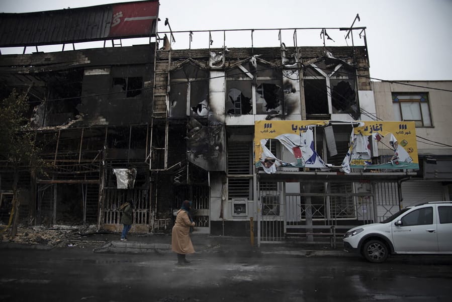 In this photo taken Monday, Nov. 18, 2019, and released by Iranian Students&#039; News Agency, ISNA, people walk past buildings which burned during protests that followed the authorities&#039; decision to raise gasoline prices, in the city of Karaj, west of the capital Tehran, Iran. An article published Tuesday in the Keyhan hard-line newspaper in Iran is suggesting that those who led violent protests will be executed by hanging as the unrest continues.