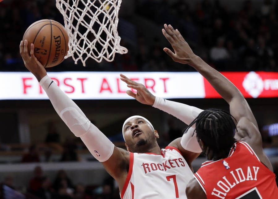 FILE - In this Nov. 3, 2018, file photo, Houston Rockets forward Carmelo Anthony, left, drives to the basket against Chicago Bulls forward Justin Holiday during the first half of an NBA basketball game in Chicago. A person familiar with the details says Anthony is returning to the NBA with the Portland Trail Blazers. The 10-time All-Star has not played since a short stint with the Rockets ended a little more than a year ago after just 10 games. (AP Photo/Nam Y.