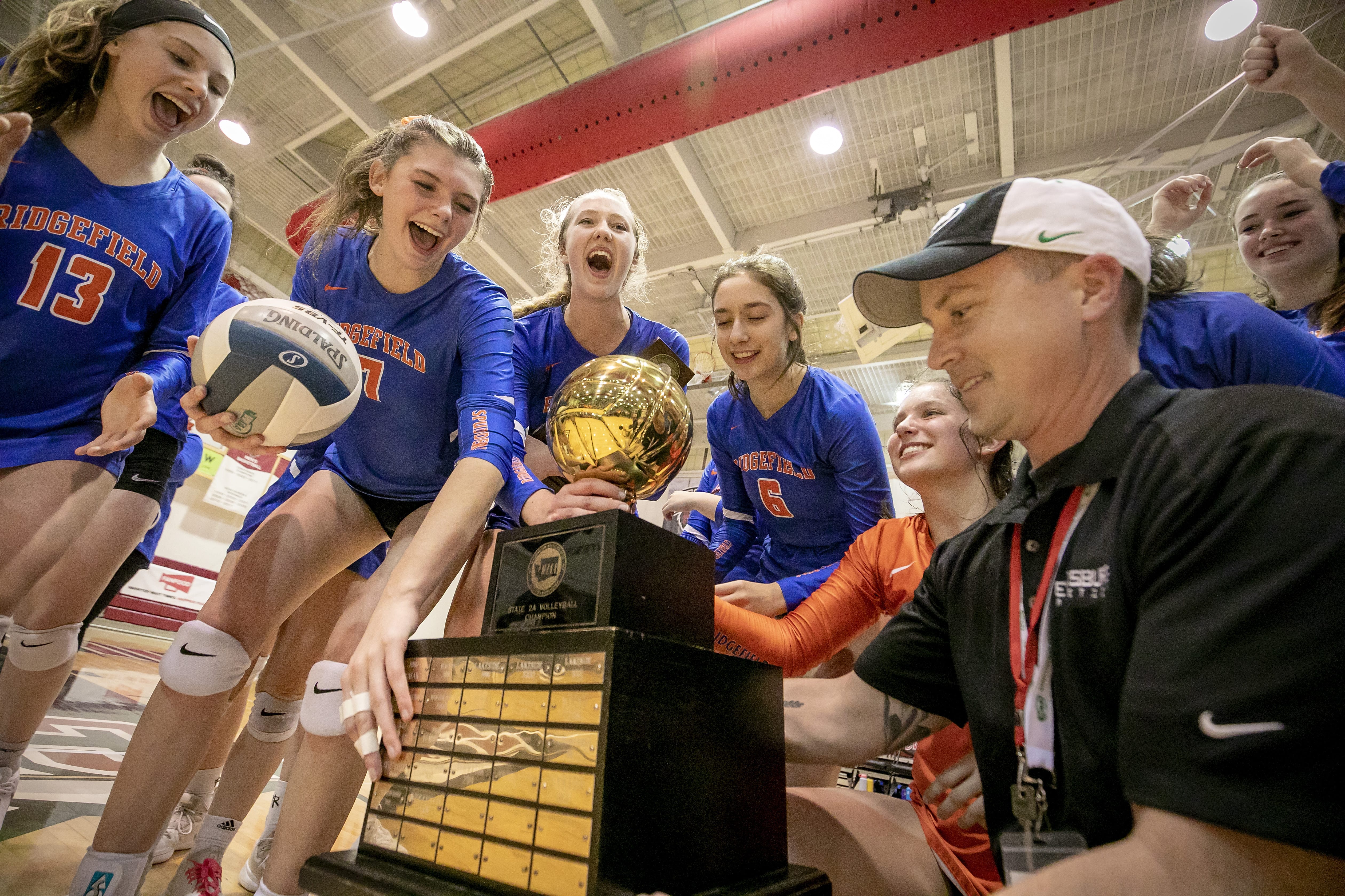 The Ridgefield High School volleyball team celebrates as Neil Musser, right, presents the WIAA 2A girls championship trophy after the Spudders defeats the Ellensburg Bulldogs 3-1 on Saturday, Nov. 16, 2019, at the Nicholson Pavilion in Ellensburg, Wash.