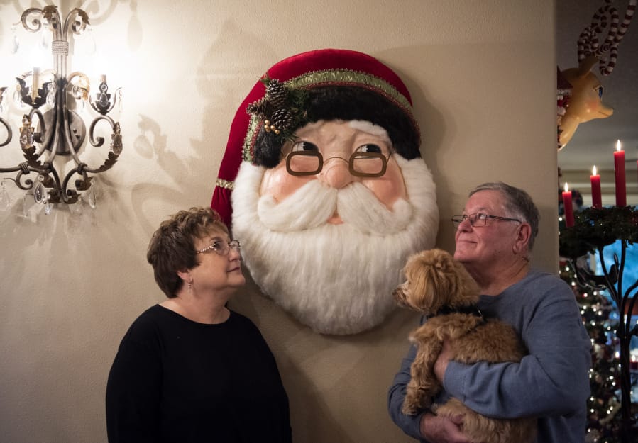 Janis and Marty Bell pose for a photo with their Havanese, Molly, in front of a Katherine&#039;s Collection wooden Santa at their home in Yacolt on Monday. Every room in the house is filled with a variety of Christmas decorations that Janis Bell has collected over the past 50 years.