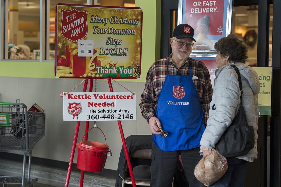 Bruce Davis of Vancouver, left, greets shopper Myrna Webb of Redmond, Ore., while bell ringing at the Grand Central Fred Meyer on Monday afternoon. Davis has been helping out as a bell ringer for the last 50 years. &quot;It&#039;s actually a lot of fun. I enjoy it,&quot; he said.