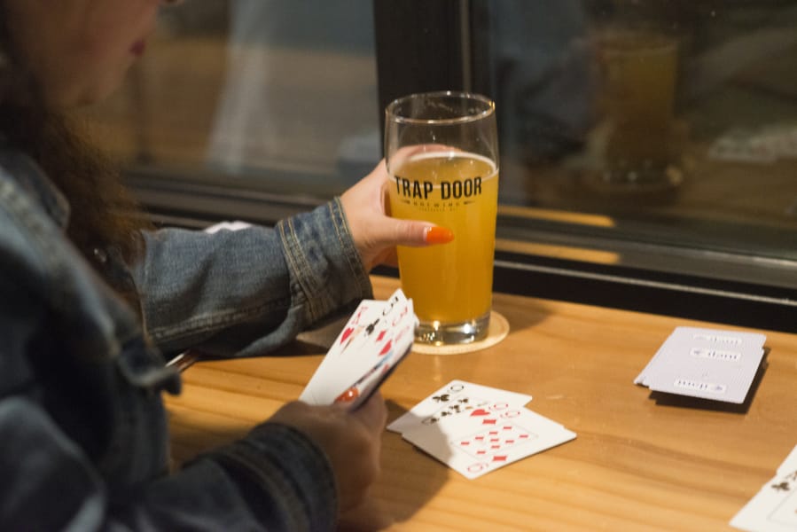 Jean Figueroa takes a drink break while playing gin rummy during a release event for MightyHighPA, a collaborative beer by Wingman Brewing, Boundary Bay Brewing and Trap Door Brewing, at Trap Door&#039;s taproom in Vancouver in October 2018. MightyHighPA is the first cannabis terpene beer produced and canned in Washington. Oregon has ruled that it will not allow cannabis-infused alcoholic beverages.