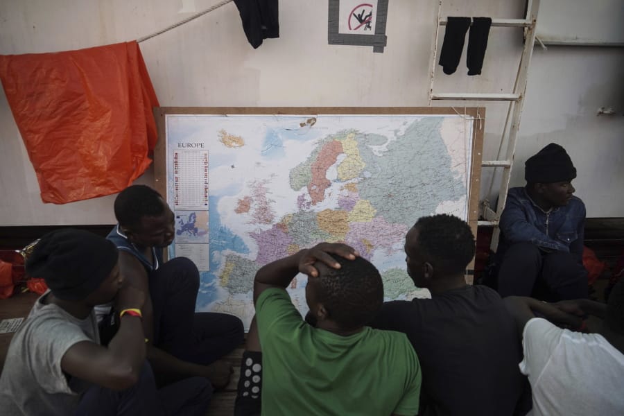 In this Sept. 23, 2019 photo, rescued migrants look at a map of Europe aboard the Ocean Viking humanitarian ship as it sails in the Mediterranean Sea. The misery of migrants in Libya has spawned a thriving and highly lucrative business, in part funded by the EU and enabled by the United Nations, an Associated Press investigation has found.