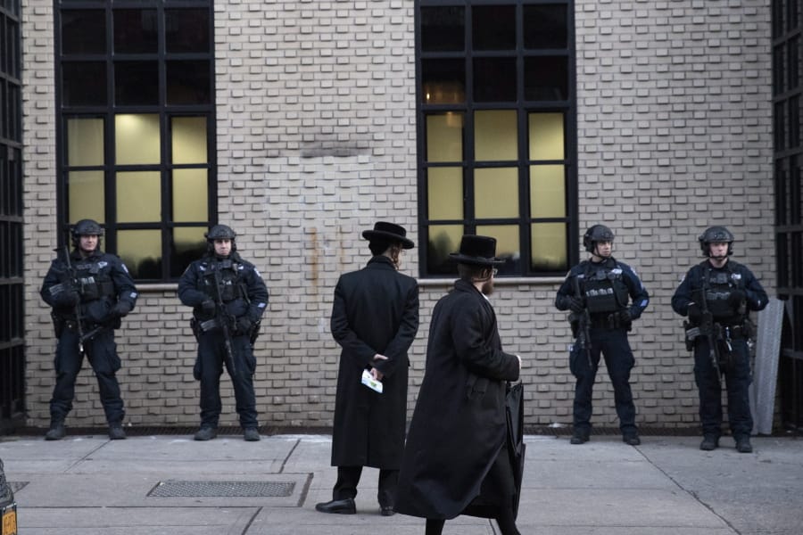 FILE - In this Dec. 11, 2019 file photo, Orthodox Jewish men pass New York City police guarding a Brooklyn synagogue prior to a funeral for Mosche Deutsch in New York. Deutsch, a rabbinical student from Brooklyn, was killed in the shooting inside a Jersey City, N.J. market. New York City is increasing its police presence in some Brooklyn neighborhoods with large Jewish populations after a number of possibly anti-Semitic attacks during the Hanukkah holiday.