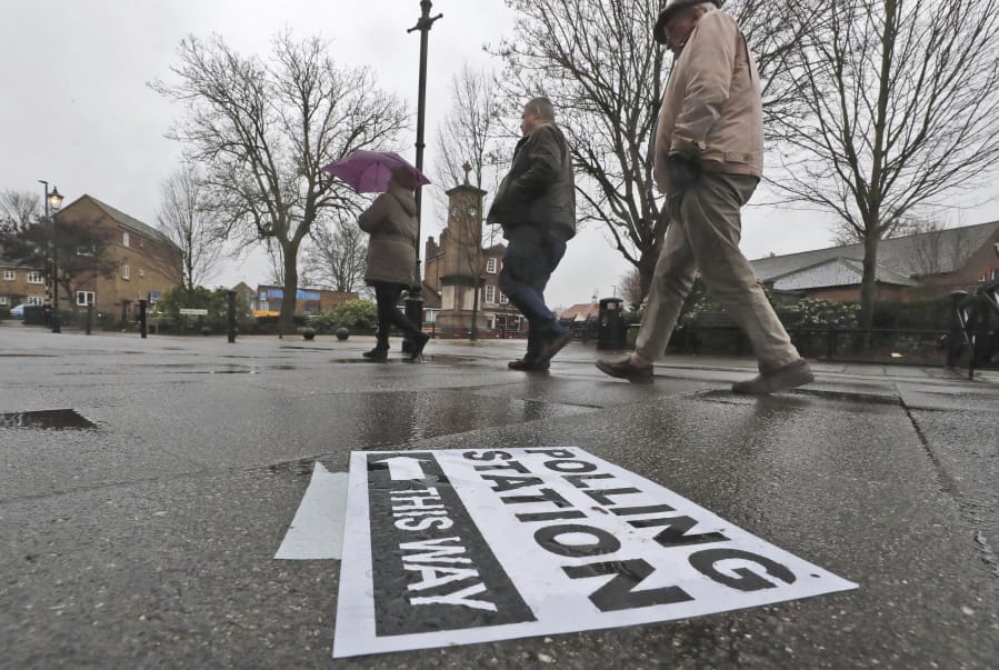 A polling station signpost lies on the pavement as voters approach a polling station in Twickenham, England, Thursday, Dec. 12, 2019. British voters are deciding who they want to resolve the Brexit conundrum in an election seen as one of the most important since the end of World War II.