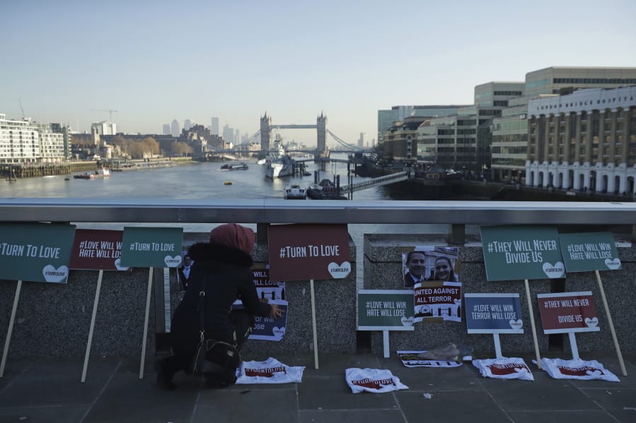 A member of the Faiths Forum for London places tributes on London Bridge in London, Monday, Dec. 2, 2019. London Bridge reopened to cars and pedestrians Monday, three days after a man previously convicted of terrorism offenses stabbed two people to death and injured three others before being shot dead by police.