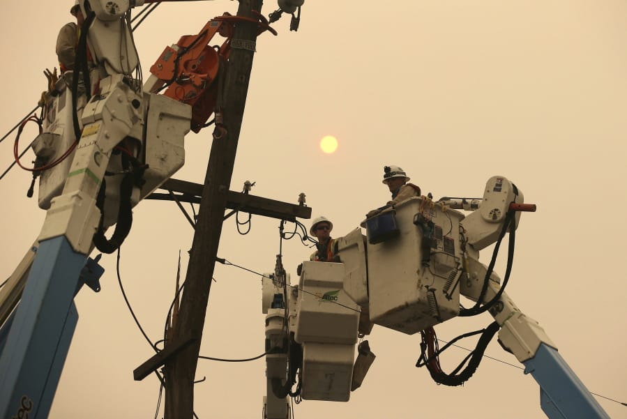 FILE - In this Nov. 9, 2018 file photo, Pacific Gas &amp; Electric crews work to restore power lines in Paradise, Calif. Pacific Gas and Electric says it has reached a $13.5 billion settlement that will resolve all major claims related to devastating wildfires blamed on its outdated equipment and negligence. The settlement, which the utility says was reached Friday, Dec. 6, 2019, still requires court approval.
