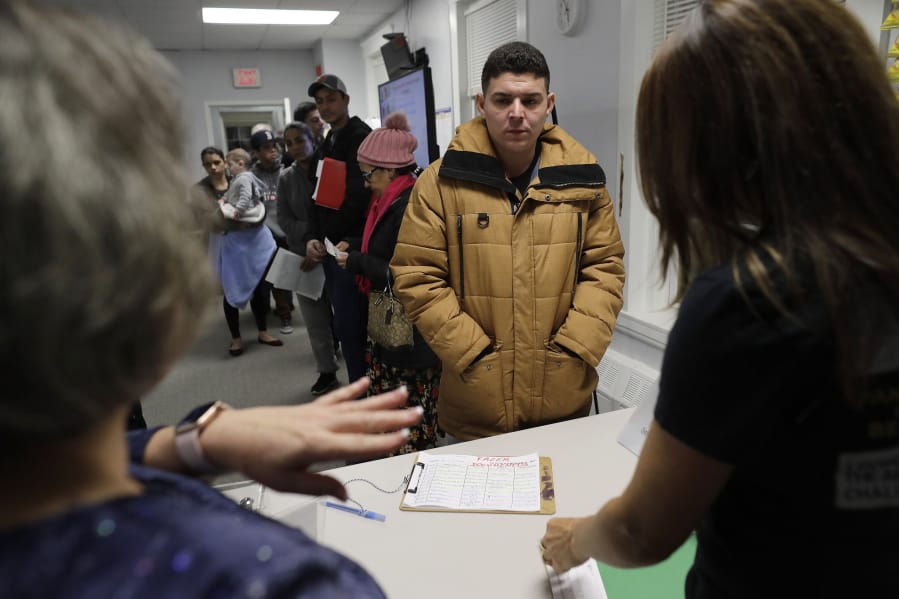 In this Wednesday, Dec. 4, 2019 photo Helison Alvarenga, of Brazil, center, speaks with volunteers Marcia Previatti, front left, and Arlene Vilela, front right, at the New England Community Center, in Stoughton, Mass. Alvarenga, a 26-year-old from the Brazilian state of Minas Gerais, arrived in Massachusetts about four months ago after crossing the Mexican border at Juarez with his 24-year-old wife, Amanda, and 6-year-old son, David. The family were at the community center Dec. 4, to apply for new Brazilian passports, which Alvarenga says were seized by border officials.