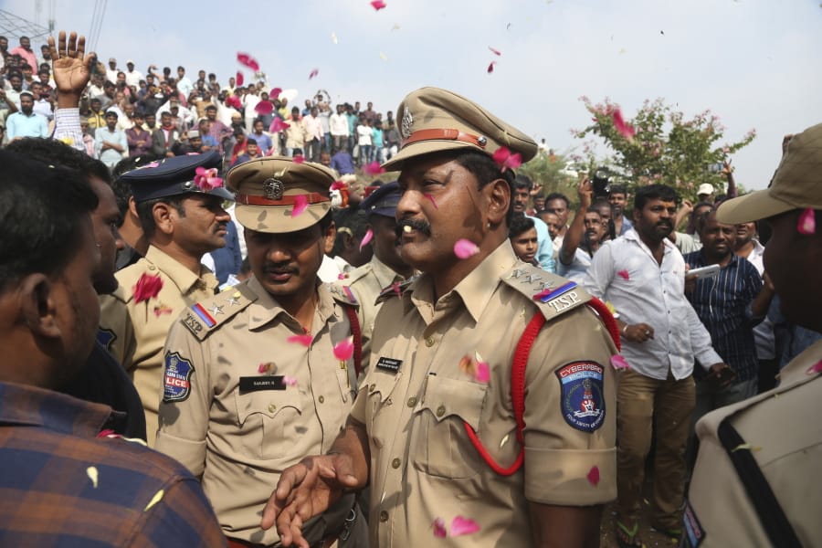 People throw flower petals on the Indian policemen guarding the area where rape accused were shot, in Shadnagar some 50 kilometers or 31 miles from  Hyderabad, India, Friday, Dec. 6, 2019. An Indian police official says four men accused of raping and killing a woman in southern India have been fatally shot by police.