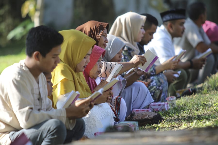 People read the holy book of the Quran as they pray at a mass grave site for the victims of the Indian Ocean tsunami, during the commemoration of the 15th anniversary of the disaster in Banda Aceh, Indonesia, Thursday, Dec. 26, 2019.
