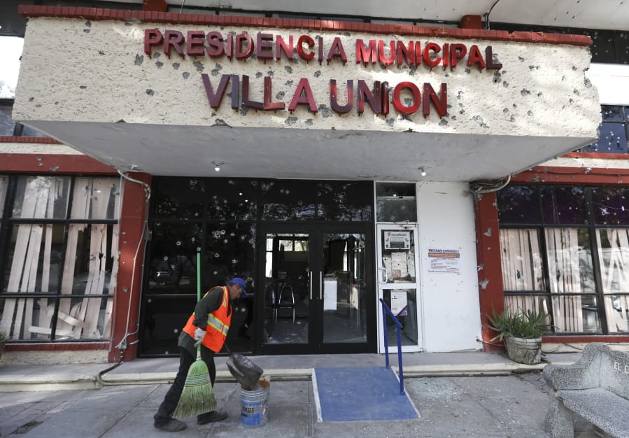 A worker cleans up Monday outside City Hall, riddled with bullet holes, in Villa Union, Mexico.