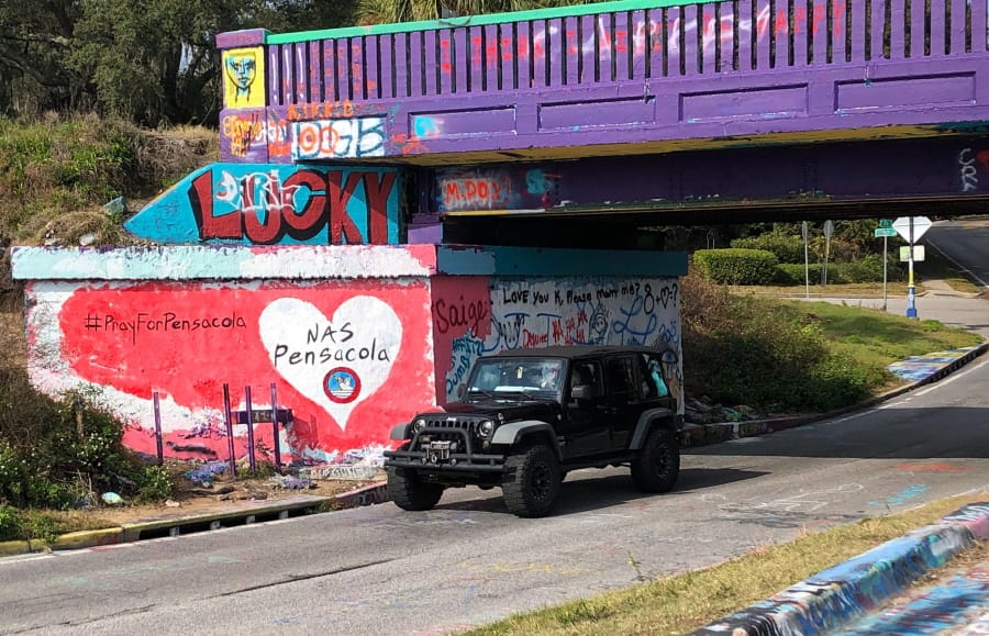 A vehicle drives by a tribute Saturday to victims of the Naval Air Station Pensacola shooting painted on what&#039;s known as Graffiti Bridge in downtown Pensacola, Fla.