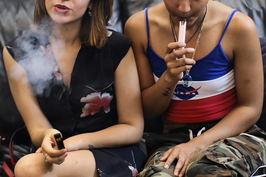 FILE - In this Saturday, June 8, 2019, file photo, two women smoke cannabis vape pens at a party in Los Angeles. On Thursday, Dec. 12, 2019, U.S. health officials said 26 states have reported deaths, for a total of 52.