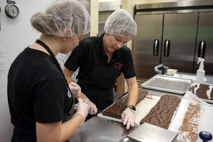 Killa Bites baker Teija Karlsen, 16, and Killa Bites co-owner Donna Suomi cut biscotti in Ridgefield. Suomi is working with employees to teach them recipes and instructions. Suomi hopes to be more hands-off in the kitchen so she can spend more time developing recipes.
