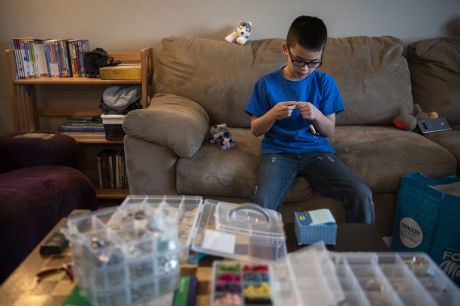 Keoni Ching, 8, demonstrates how he makes keychains Friday morning at his home in Battle Ground. Last month, Keoni started making keychains to raise money to pay off students&#039; unpaid lunch accounts at his school, Benjamin Franklin Elementary School. He&#039;s raised nearly $1,000.