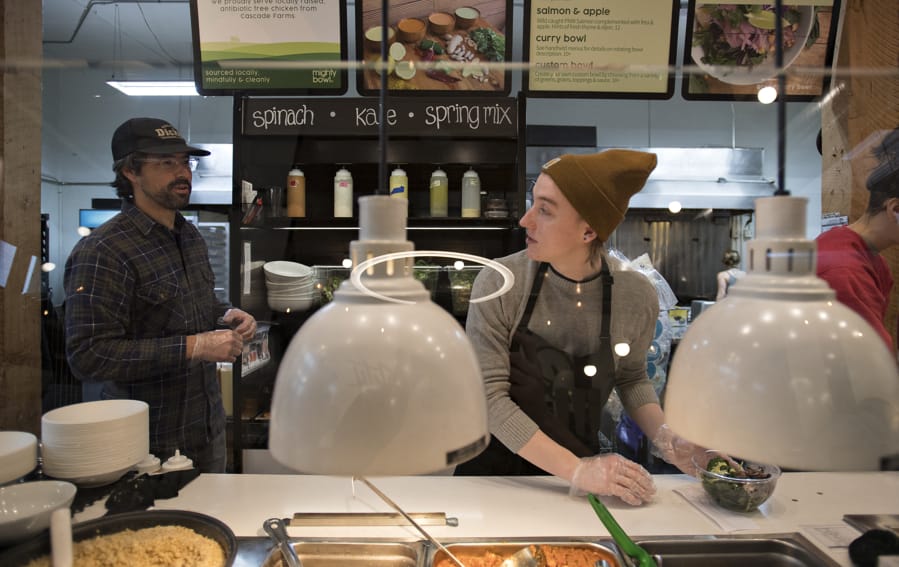 Steve Valenta, left, owner of The Mighty Bowl in downtown Vancouver, talks with employee Elias Gribble while preparing for the lunch rush on Wednesday. Gribble is one of the employees who recently received a minimum-wage increase.