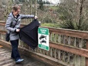 Andrea Logue, a program coordinator for outreach and education with Clark County&#039;s Clean Water Division, unveils the first installed sign featuring the new watershed design, on the footbridge over Salmon Creek at Klineline Pond.