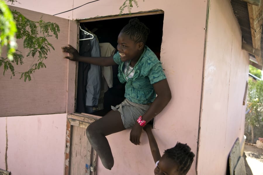 In this Jan. 3, 2020 photo, Rose-Berline Thomas sits in a window to speak with her mother outside at their home in Canaan, a district in Croix des Bouquets, Haiti, created for people who lost their homes in the earthquake 10 years ago. Rose-Berline Thomas was 2-years-old when the earthquake collapsed her family&#039;s home on top of her, crushing her foot.