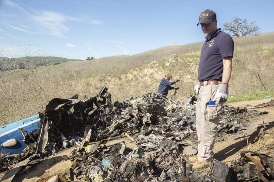 In this image taken Monday, Jan. 27, 2020, and provided by the National Transportation Safety Board, NTSB investigators Adam Huray, right, and Carol Hogan examine wreckage as part of the NTSB&#039;s investigation of a helicopter crash near Calabasas, Calif. The Sunday, Jan.