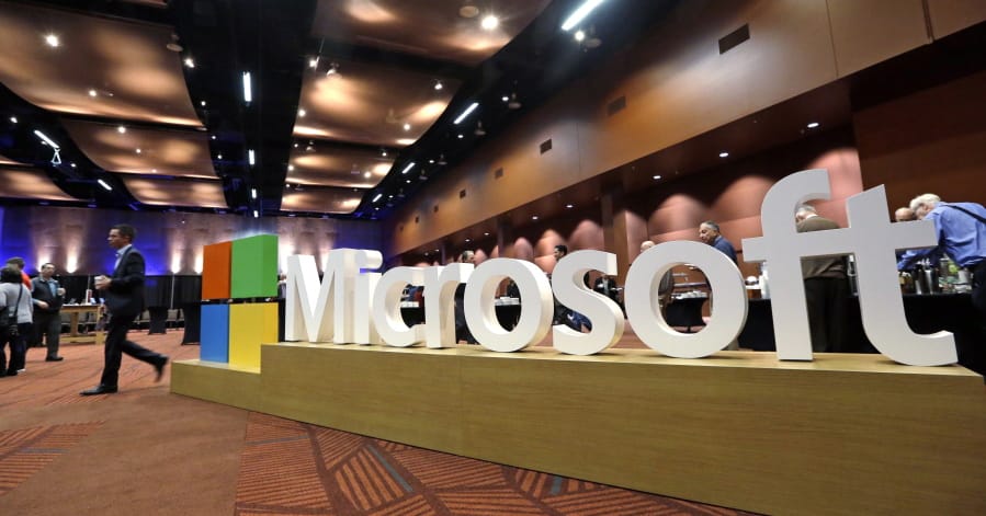 FILE - In this Nov. 30, 2016, file photo a man walks past a Microsoft sign at the annual Microsoft shareholders meeting in Bellevue, Wash. Microsoft on Thursday, Jan. 16, 2020, is announcing a plan to reduce its carbon footprint.