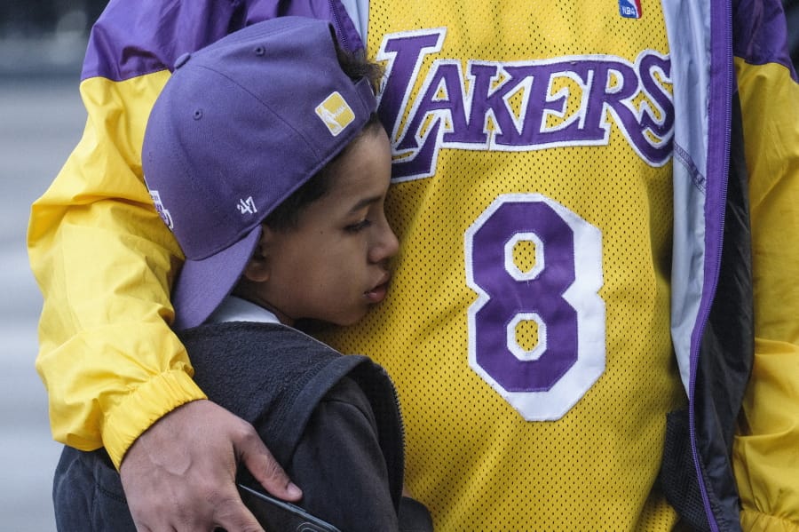 Eric Mascarenhas comforts his son Nicolas at a memorial for Kobe Bryant near Staples Center Monday, Jan. 27, 2020, in Los Angeles. Bryant, the 18-time NBA All-Star who won five championships and became one of the greatest basketball players of his generation during a 20-year career with the Los Angeles Lakers, died in a helicopter crash Sunday. (AP Photo/Ringo H.W.