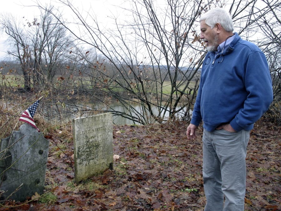In this Dec. 10, 2019, photo, Don Mason, chairman of the Weybridge, Vt., selectboard looks at gravestone of Revolutionary War soldier William Haven, who is buried in a cemetery near the edge of an eroding river bank in Weybridge, Vt. Rising seas, erosion and flooding from worsening storms that some scientists believe are caused by climate change are putting some older graveyards across the country at risk.
