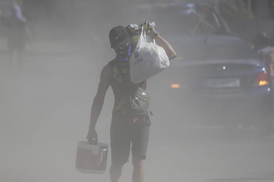 A man walks the his belongings through clouds of ash kicked up on a road as authorities enforced total evacuation of residents living near Taal volcano in Agoncillo town, Batangas province, southern Philippines on Thursday Jan. 16, 2020. Taal volcano belched smaller plumes of ash Thursday but shuddered continuously with earthquakes and cracked roads in nearby towns, which were blockaded by police due to fears of a bigger eruption.