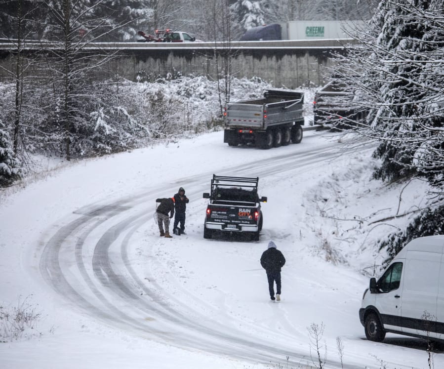 A driver starts to put on chains in compact snow and ice on the NE 72nd Place on-ramp to Highway 405 in Kirkland, Wash., Monday, Jan. 13, 2020.
