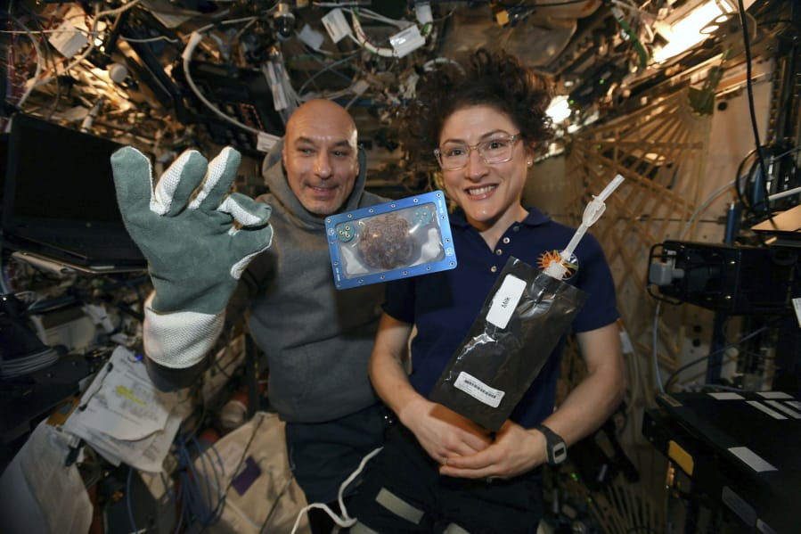 In this photo made available by U.S. astronaut Christina Koch via Twitter on Dec. 26, she and Italian astronaut Luca Parmitano pose for a photo with a cookie baked on the International Space Station.