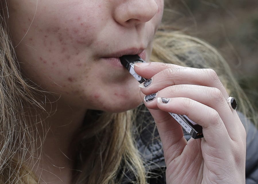 FILE - In this April 11, 2018, file photo, a high school student uses a vaping device near a school campus in Cambridge, Mass. The Trump administration announced Thursday that it will prohibit fruit, candy, mint and dessert flavors from small, cartridge-based e-cigarettes that are popular with high school students. But menthol and tobacco-flavored e-cigarettes will be allowed to remain on the market.
