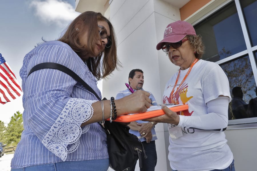 In this Dec. 10, 2019 photo, Hispanic Federation Canvasser Ana M. Vigo, right, registers Maria Moralez, left, to vote as Ivan Baez Munoz looks on outside the Polk Coutny Tax Collectors office in Davenport, Fla.