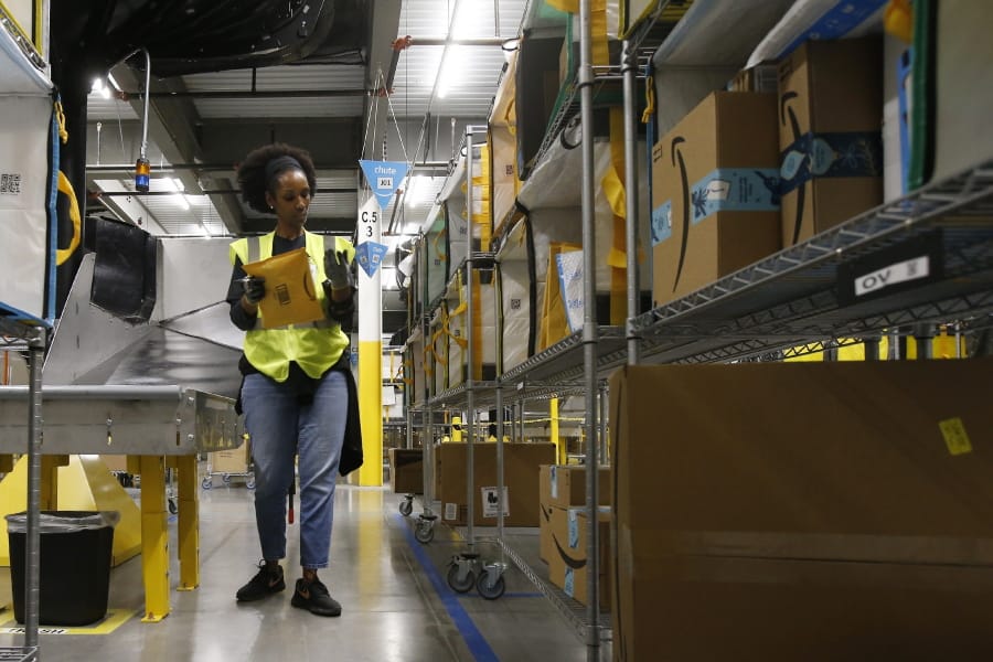 In this Dec. 17, 2019, photo Tahsha Sydnor stows packages into special containers after Amazon robots deliver separated packages by zip code at an Amazon warehouse facility in Goodyear, Ariz. Amazon and its rivals are increasingly requiring warehouse employees to get used to working with robots. The company now has more than 200,000 robotic vehicles it calls &quot;drives&quot; that are moving goods through its delivery-fulfillment centers around the U.S.  (AP Photo/Ross D.