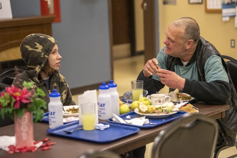 Donnie Rousey, 14, left, eats dinner with Mark Traxler, who is homeless and lives in Washougal, during Refuel Washougal&#039;s free weekly meal at the Washougal Community Center.