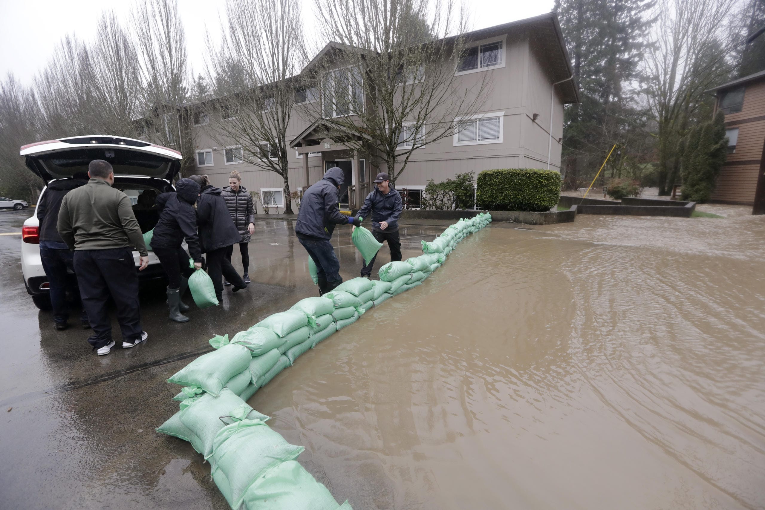 Residents and volunteers work to place sandbags at an apartment complex as flood waters rise Thursday, Feb. 6, 2020, in Issaquah, Wash. Heavy rain sent the creek over a major roadway, under an apartment building east of Seattle and up to the foundations of homes as heavy rains pounded the region. A flood watch was in effect through Friday afternoon across most of western Washington. Numerous roads were closed because of water over the roadway. Officials also warned of landslide risks.