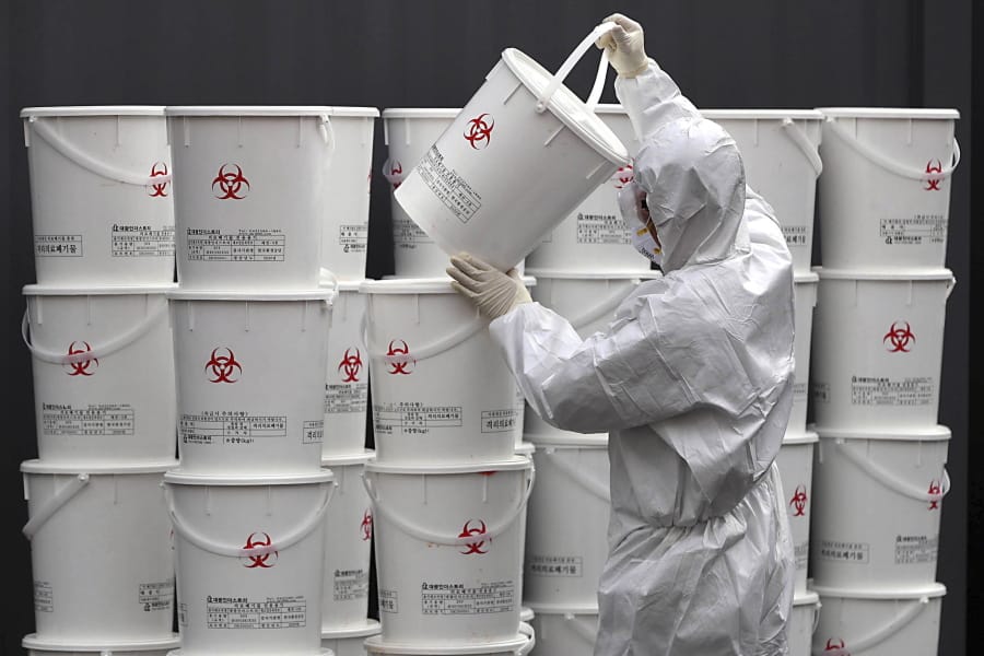 A worker in protective gear stacks plastic buckets containing medical waste from coronavirus patients at a medical center in Daegu, South Korea, Monday, Feb. 24, 2020. South Korea reported another large jump in new virus cases Monday a day after the the president called for &quot;unprecedented, powerful&quot; steps to combat the outbreak that is increasingly confounding attempts to stop the spread.