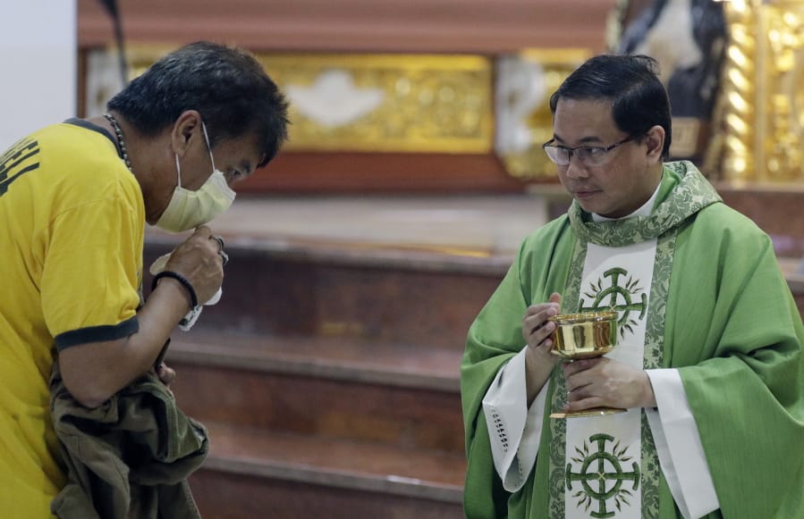 Catholic priest Father Joseph Arellano, right, watches a man who forgot to take off his protective mask and tried to insert the host in his mouth during a Mass on Feb. 10 at the Minor Basilica of San Lorenzo Ruiz in Manila, Philippines.